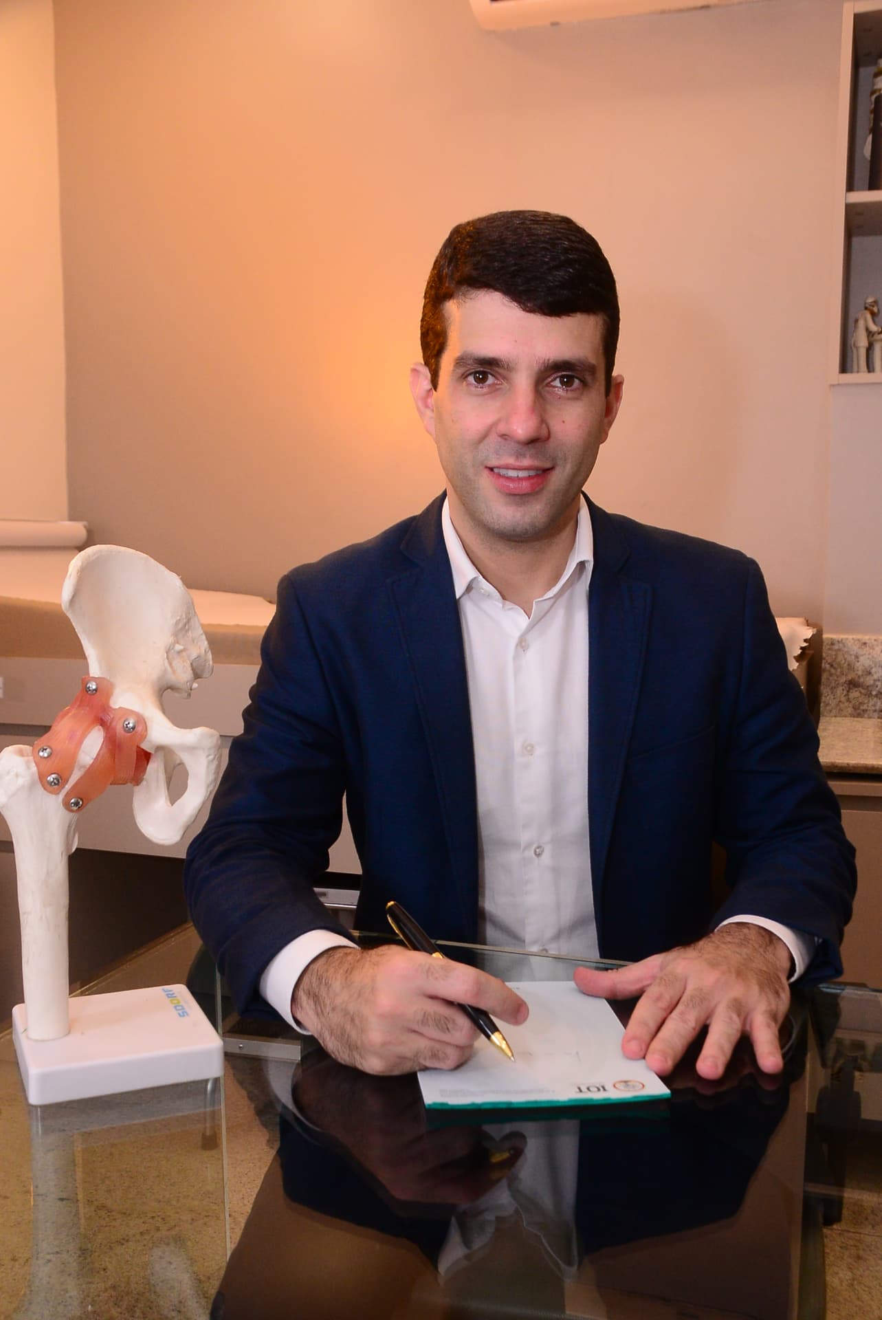 Dr. Alessandro Cavalcante no consultório ao lado de um modelo anatômico do quadril